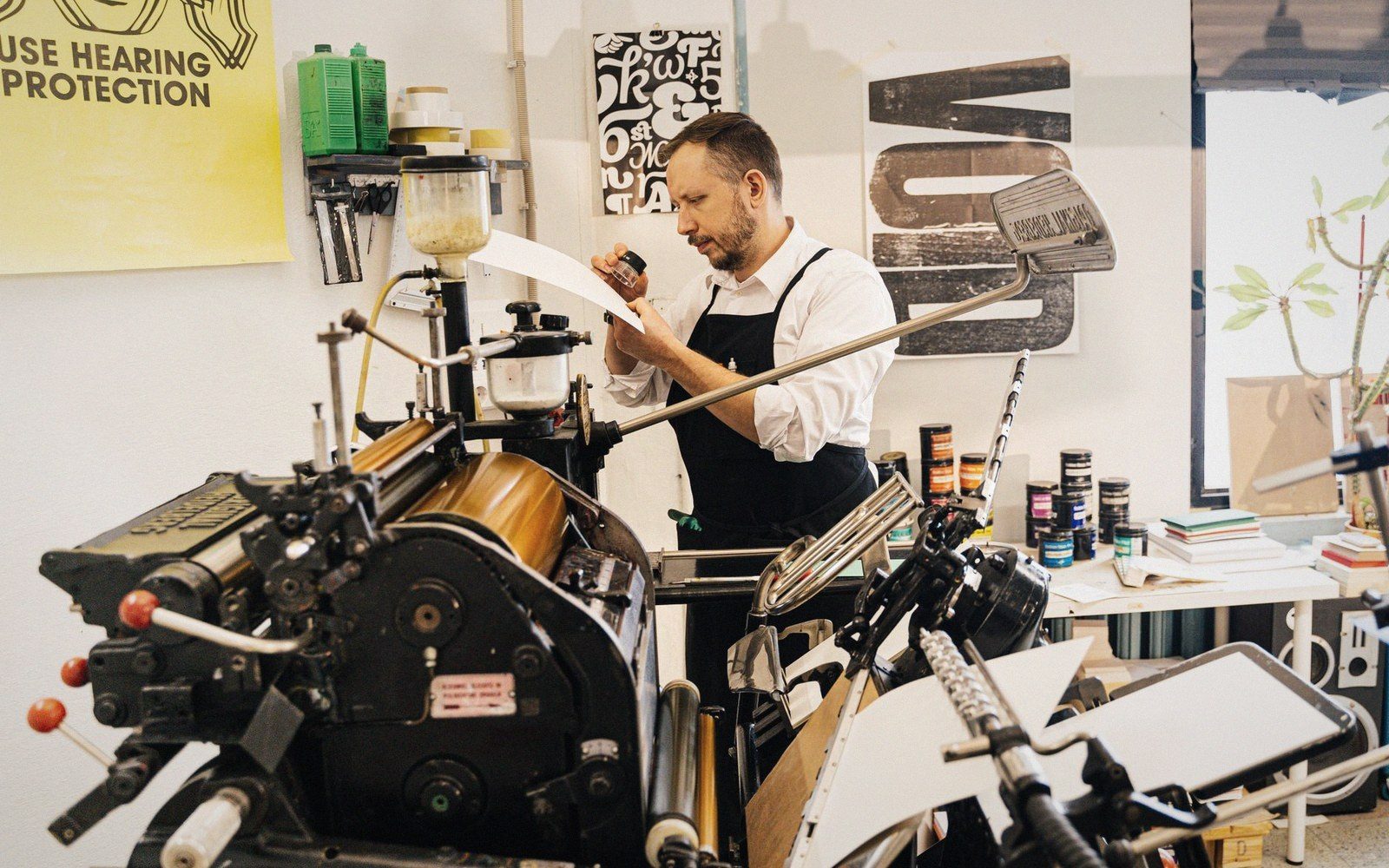 A man inspects a printed sheet beside a vintage letterpress machine in a print studio